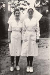 A pair of proud women nurses in belted and buttoned uniforms posing in the hospital grounds. Date unknown